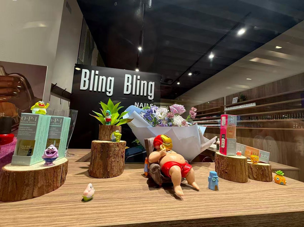 A storefront window display for Bling Bling with wooden elements, colorful flowers, and decorative items arranged on a wooden floor.